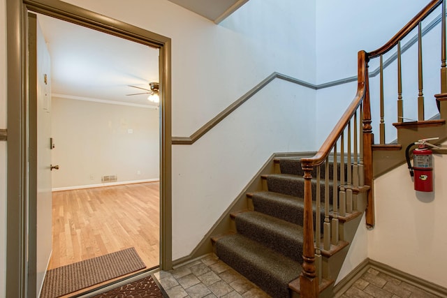 staircase with wood finished floors, visible vents, baseboards, ceiling fan, and ornamental molding