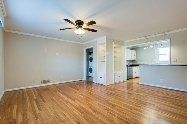 unfurnished room with visible vents, stacked washer and dryer, light wood-style flooring, crown molding, and baseboards