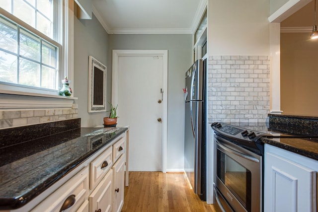 kitchen with stainless steel appliances, light wood-style floors, dark stone counters, and ornamental molding