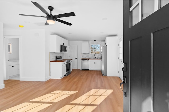 kitchen featuring light wood finished floors, decorative backsplash, appliances with stainless steel finishes, and white cabinetry