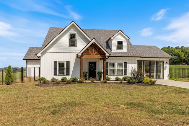 modern farmhouse featuring a front yard, roof with shingles, driveway, and fence