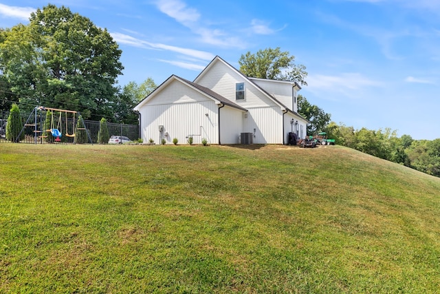 view of side of property with a playground, a yard, central AC unit, and fence