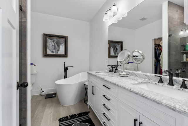 full bathroom with a spacious closet, a shower stall, wood finished floors, and a sink