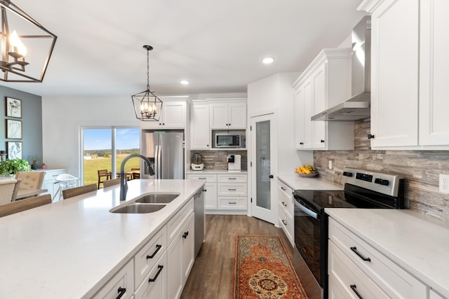 kitchen with a sink, appliances with stainless steel finishes, wall chimney exhaust hood, an inviting chandelier, and light countertops