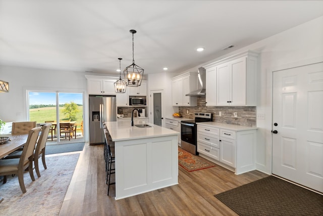 kitchen featuring a sink, decorative backsplash, light countertops, stainless steel appliances, and wall chimney range hood