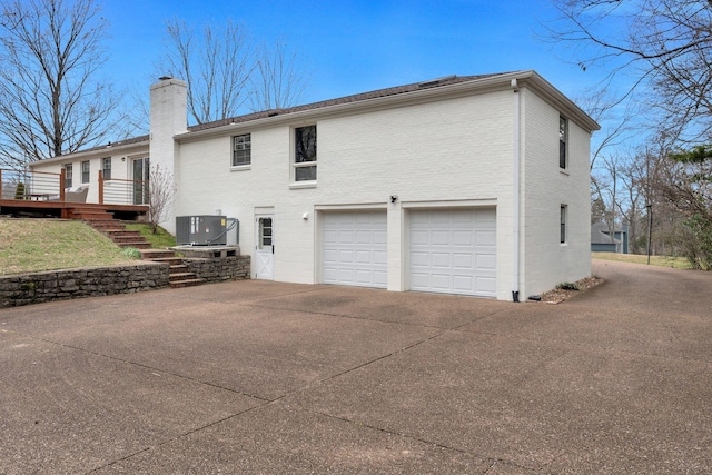 rear view of house with brick siding, an attached garage, stairs, a chimney, and driveway