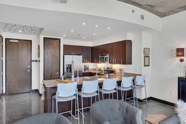 kitchen featuring visible vents, dark brown cabinets, light stone countertops, appliances with stainless steel finishes, and a peninsula