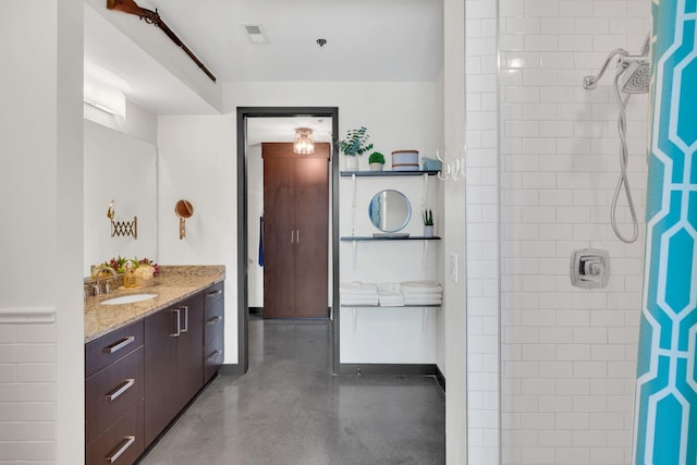 full bath featuring vanity, visible vents, baseboards, concrete floors, and a tile shower