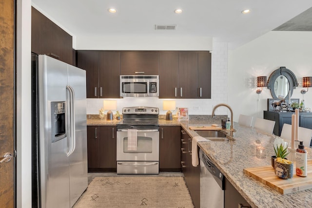 kitchen featuring a sink, light stone counters, dark brown cabinetry, and appliances with stainless steel finishes