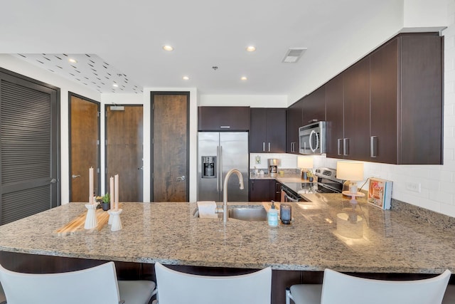 kitchen with a kitchen bar, light stone countertops, appliances with stainless steel finishes, and a peninsula