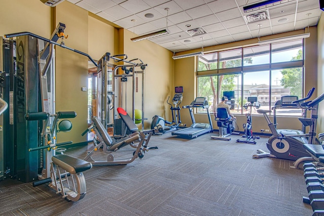 exercise room with a high ceiling, a paneled ceiling, visible vents, and carpet floors