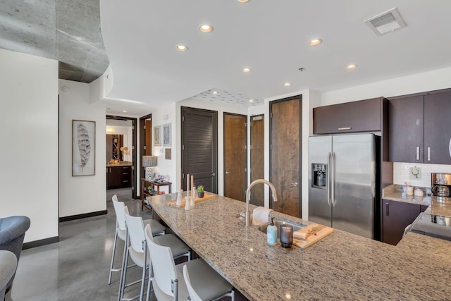 kitchen with visible vents, stainless steel refrigerator with ice dispenser, a sink, light stone counters, and decorative backsplash