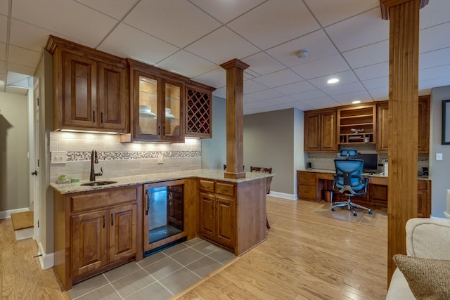 kitchen with beverage cooler, built in study area, open shelves, decorative columns, and a sink