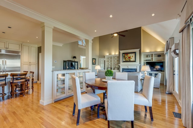 dining room with a ceiling fan, a fireplace, light wood-type flooring, and ornate columns