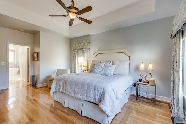 bedroom with baseboards, a raised ceiling, light wood-style floors, and a ceiling fan