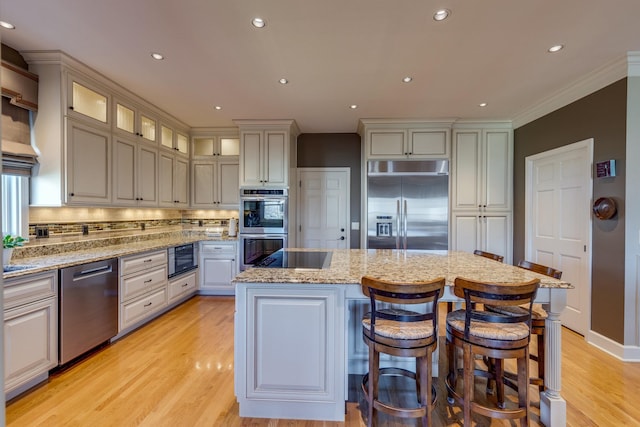 kitchen with light stone countertops, light wood finished floors, a kitchen island, decorative backsplash, and appliances with stainless steel finishes