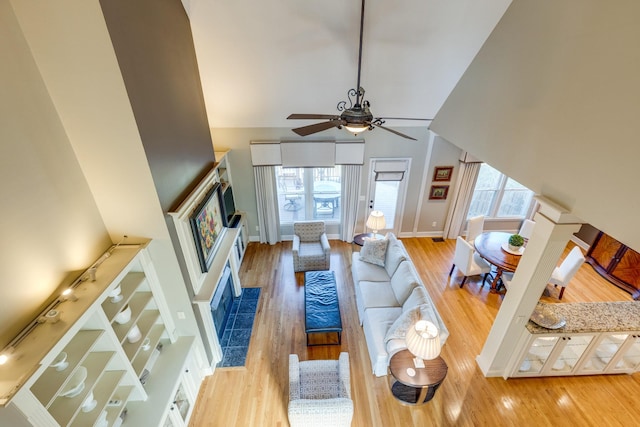 living area with a ceiling fan, wood finished floors, baseboards, and high vaulted ceiling