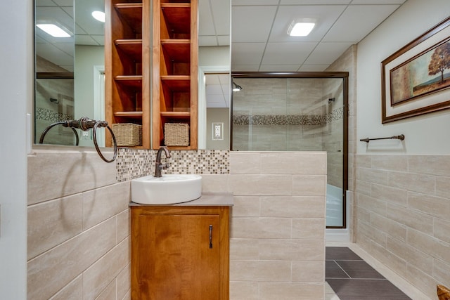 full bathroom with a stall shower, tile walls, vanity, and a paneled ceiling