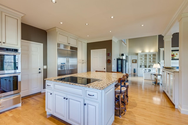 kitchen with a warming drawer, light wood-type flooring, a center island, stainless steel appliances, and ornate columns