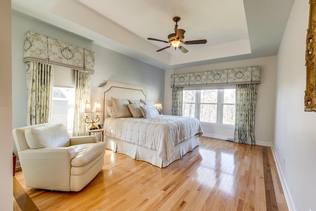 bedroom featuring baseboards, light wood-style floors, a tray ceiling, and a ceiling fan