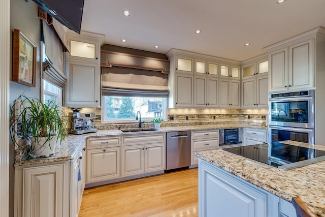 kitchen with a sink, light stone counters, appliances with stainless steel finishes, light wood finished floors, and decorative backsplash