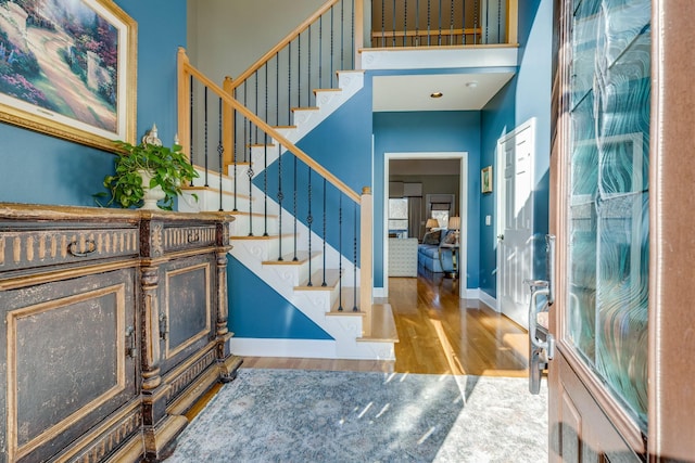 foyer entrance with stairs, a high ceiling, wood finished floors, and baseboards