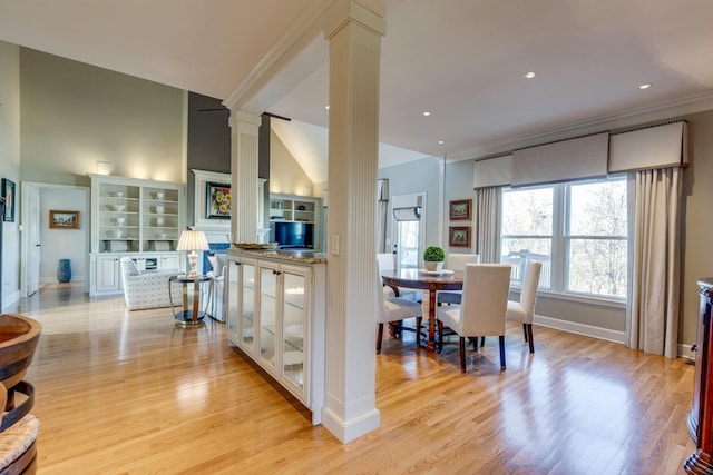 dining space with decorative columns, baseboards, light wood-style floors, and ornamental molding