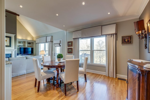 dining area featuring lofted ceiling, a high end fireplace, crown molding, light wood finished floors, and baseboards