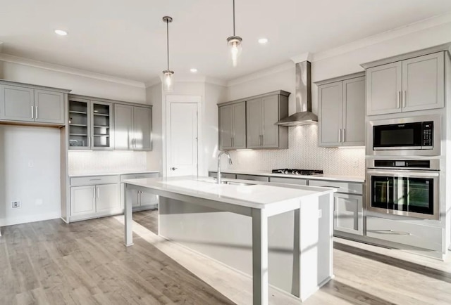 kitchen with gray cabinets, a sink, light countertops, appliances with stainless steel finishes, and wall chimney range hood