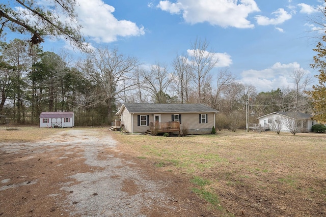 view of front facade featuring a wooden deck, a storage shed, an outdoor structure, and driveway