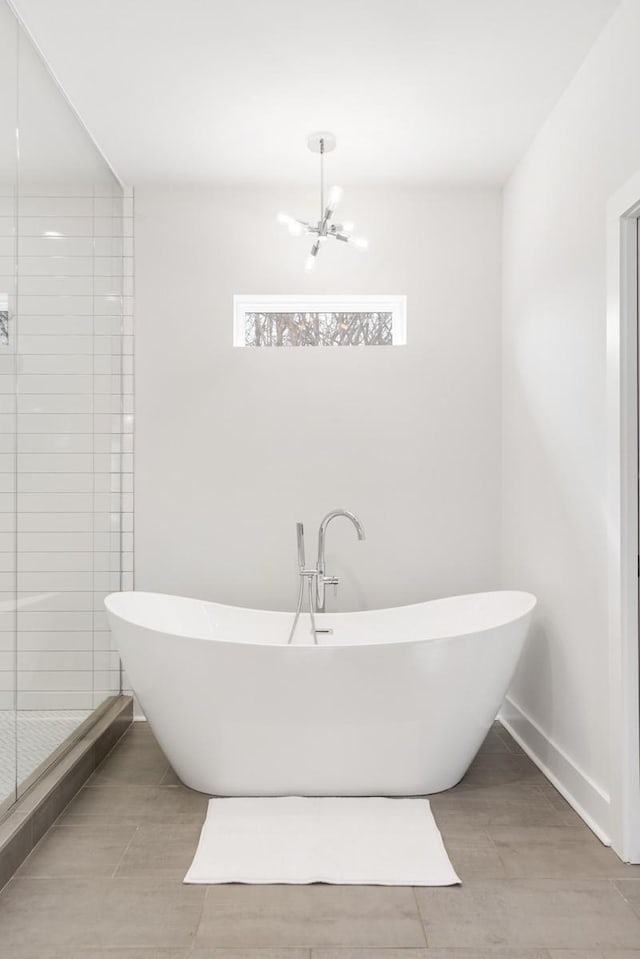 bathroom with an inviting chandelier, a shower stall, a freestanding tub, and baseboards