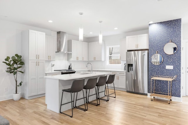 kitchen with a breakfast bar, an island with sink, a sink, stainless steel fridge, and wall chimney exhaust hood