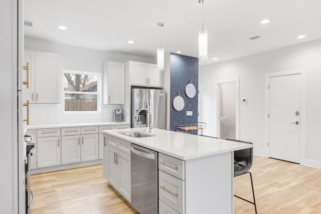 kitchen featuring stainless steel appliances, a breakfast bar, light countertops, and light wood finished floors