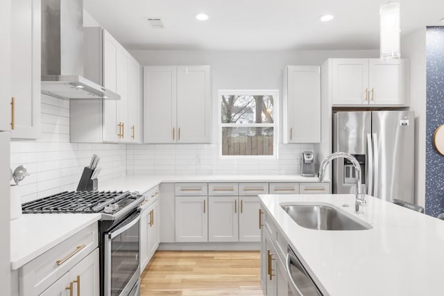 kitchen featuring a sink, light countertops, appliances with stainless steel finishes, wall chimney exhaust hood, and light wood-type flooring