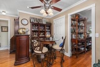 bar featuring light wood-style flooring, baseboards, crown molding, and ceiling fan