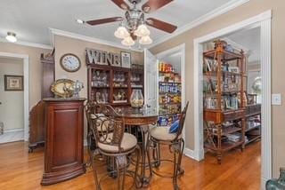 bar with ornamental molding, baseboards, ceiling fan, and wood finished floors