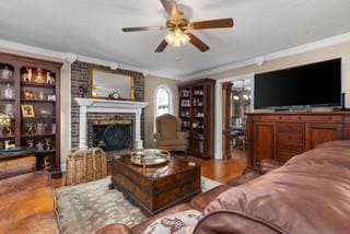 living room with a brick fireplace, wood finished floors, a ceiling fan, and ornamental molding