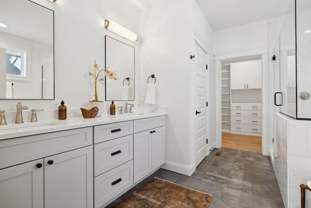 full bath with double vanity, a stall shower, a walk in closet, and a sink