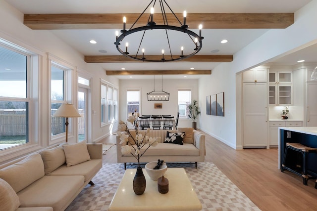 living room with beamed ceiling, baseboards, light wood-type flooring, and a chandelier