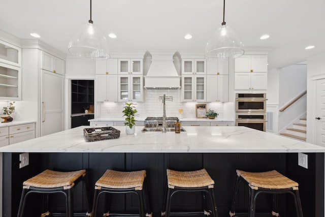 kitchen featuring custom exhaust hood, stainless steel double oven, white cabinets, and a large island