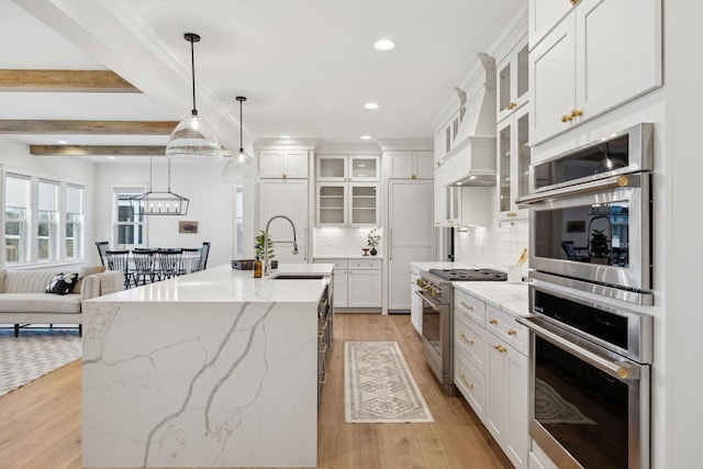 kitchen with decorative backsplash, appliances with stainless steel finishes, light wood-style floors, white cabinetry, and a kitchen island with sink