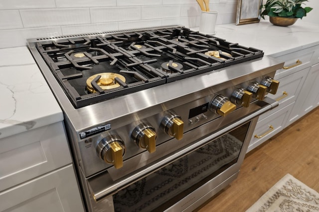 interior details with white cabinets, light wood-style floors, tasteful backsplash, and high end stainless steel range