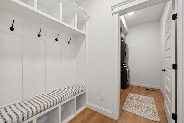 mudroom with light wood-type flooring, baseboards, and stacked washer / dryer