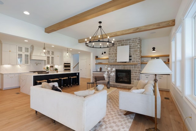 living room featuring visible vents, beam ceiling, stairway, light wood-style floors, and a stone fireplace