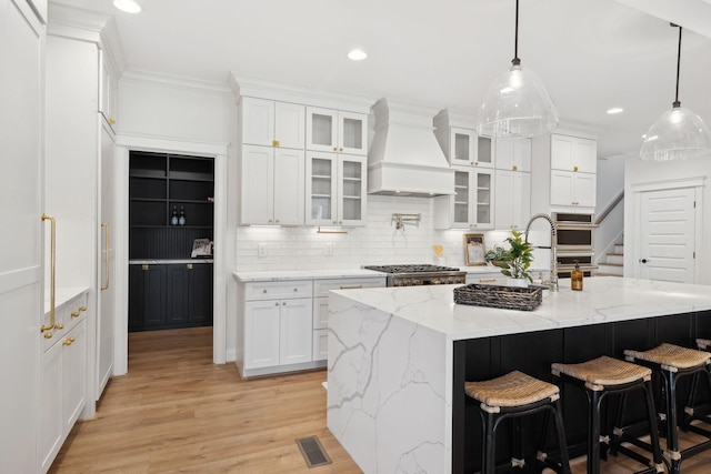 kitchen with a breakfast bar, light wood-style flooring, custom range hood, white cabinets, and tasteful backsplash