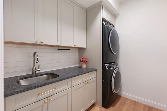 laundry room with baseboards, cabinet space, a sink, stacked washer and clothes dryer, and light wood-type flooring