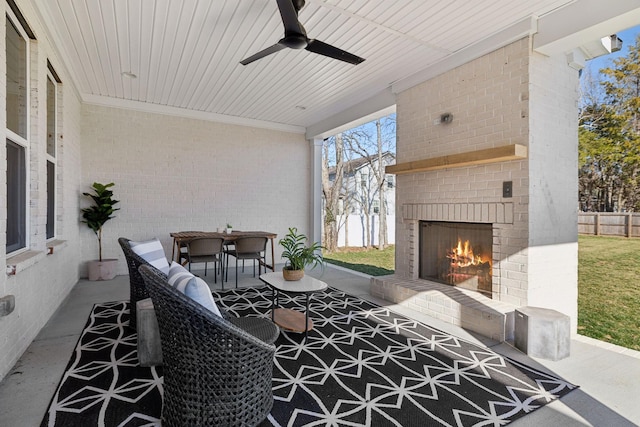 view of patio featuring fence, outdoor dining space, a ceiling fan, and an outdoor brick fireplace