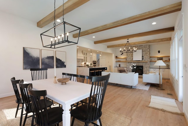 dining room featuring light wood-type flooring, beam ceiling, an inviting chandelier, and a fireplace