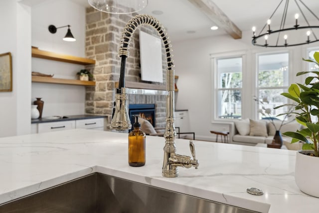 interior details featuring light stone countertops, beam ceiling, recessed lighting, a glass covered fireplace, and white cabinetry