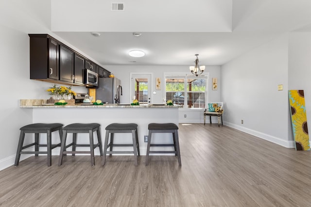 kitchen featuring visible vents, an inviting chandelier, a peninsula, stainless steel appliances, and light wood-type flooring